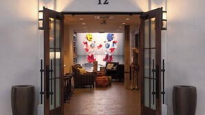 En hotelindgang med en trædør, nummer '12' over døren, og et receptionsområde med siddepladser og en væg pyntet med røde og blå balloner.