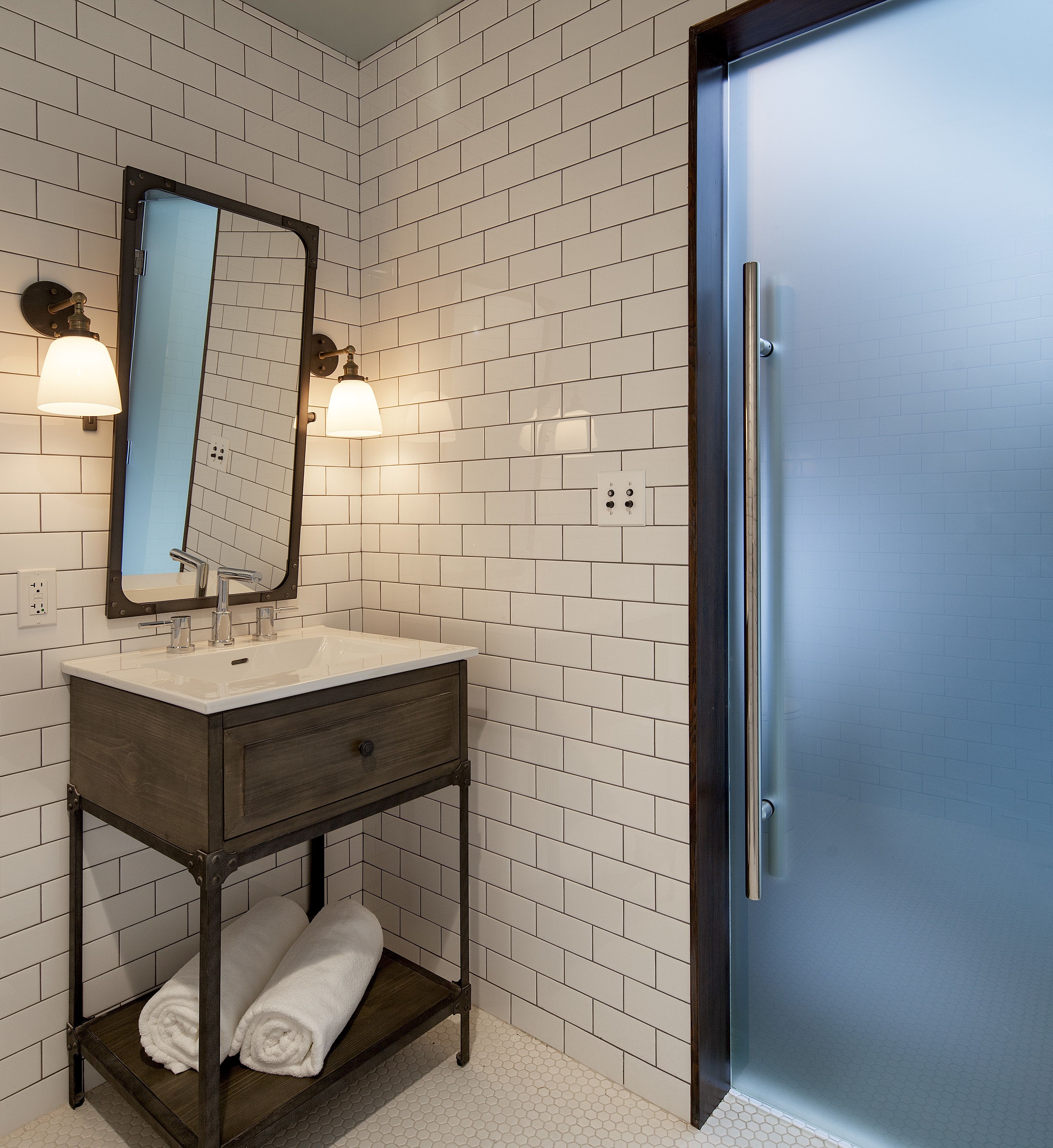 A bathroom with a white-tiled wall, a dark wooden vanity with a mirror, two wall-mounted lights, and a blue door.