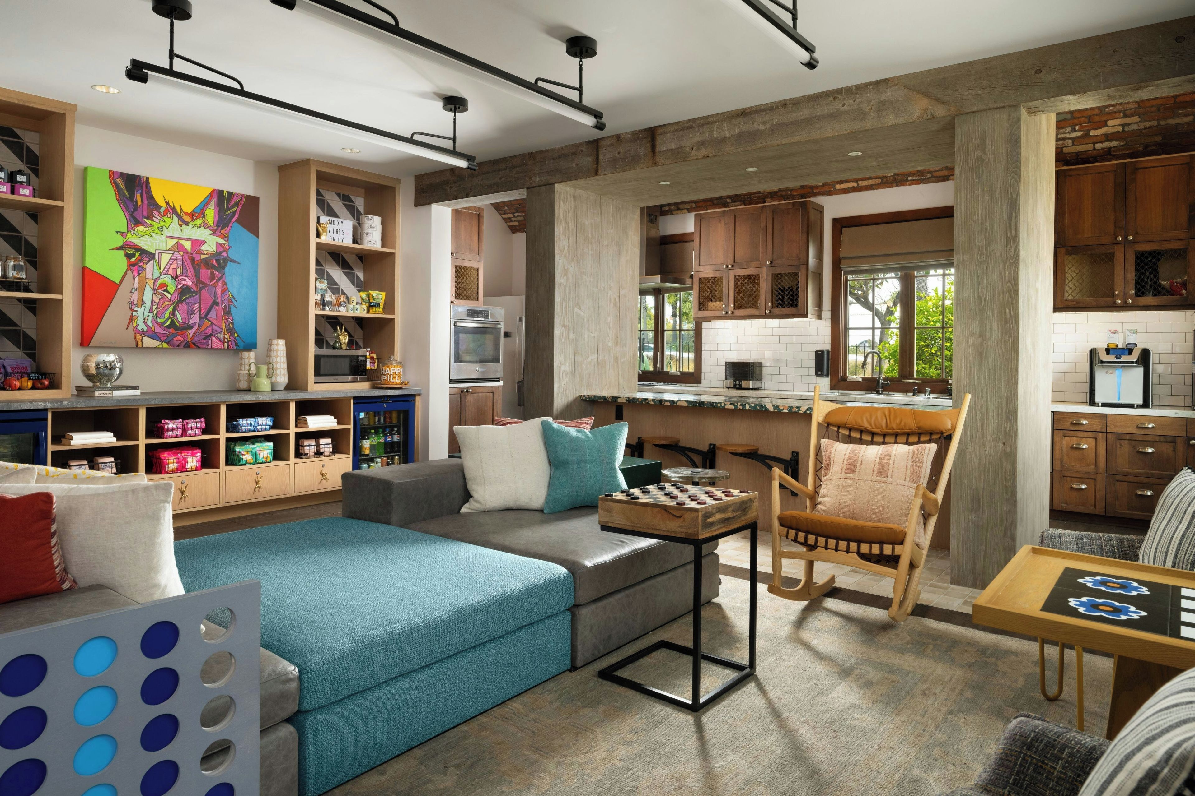 A modern living room with a sofa, a coffee table, and a chess table. There is a kitchen area with wooden cabinets and a window.