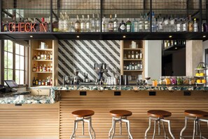 A bar area with a check-in sign, shelves of liquor bottles, a coffee machine, and bar stools.