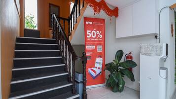 A hotel interior with a staircase, a promotional banner, a refrigerator, and a potted plant.