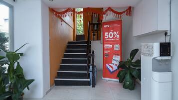 A hotel reception area with a staircase, a promotional banner, a water dispenser, and potted plants.