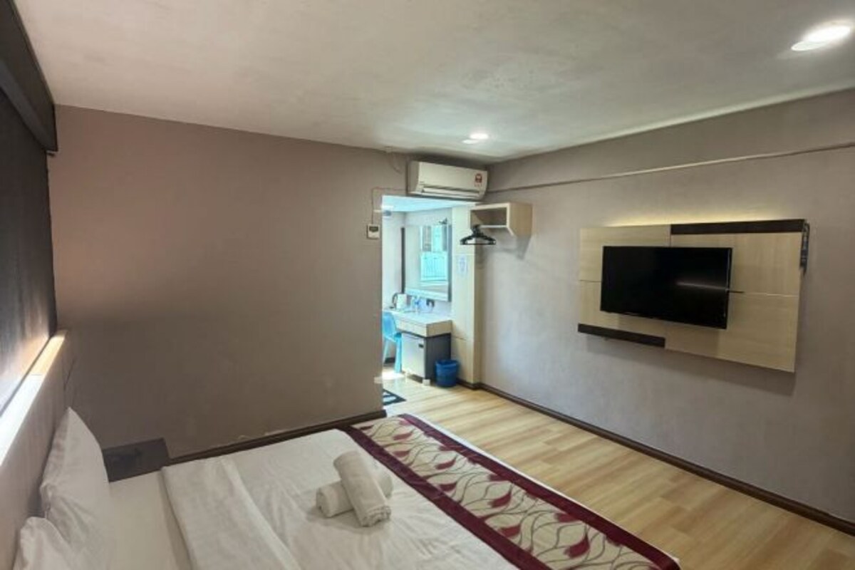Habitación de hotel con una cama, un televisor montado en la pared y un baño pequeño visible a través de una puerta abierta.