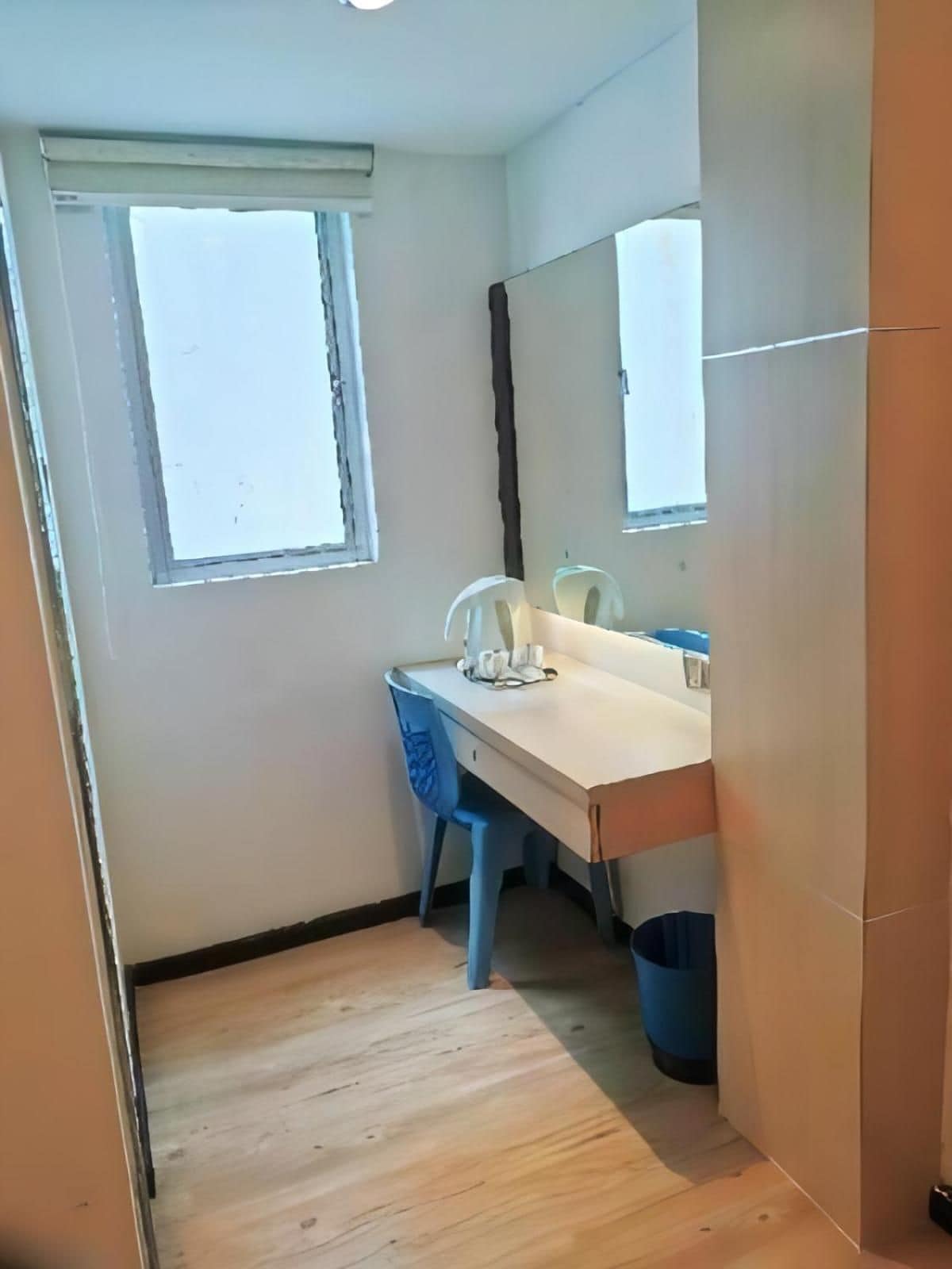 A small room with a wooden floor, a desk with a chair, a window, and a mirror.