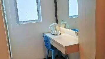 A small room with a wooden floor, a desk with a chair, a window, and a mirror.
