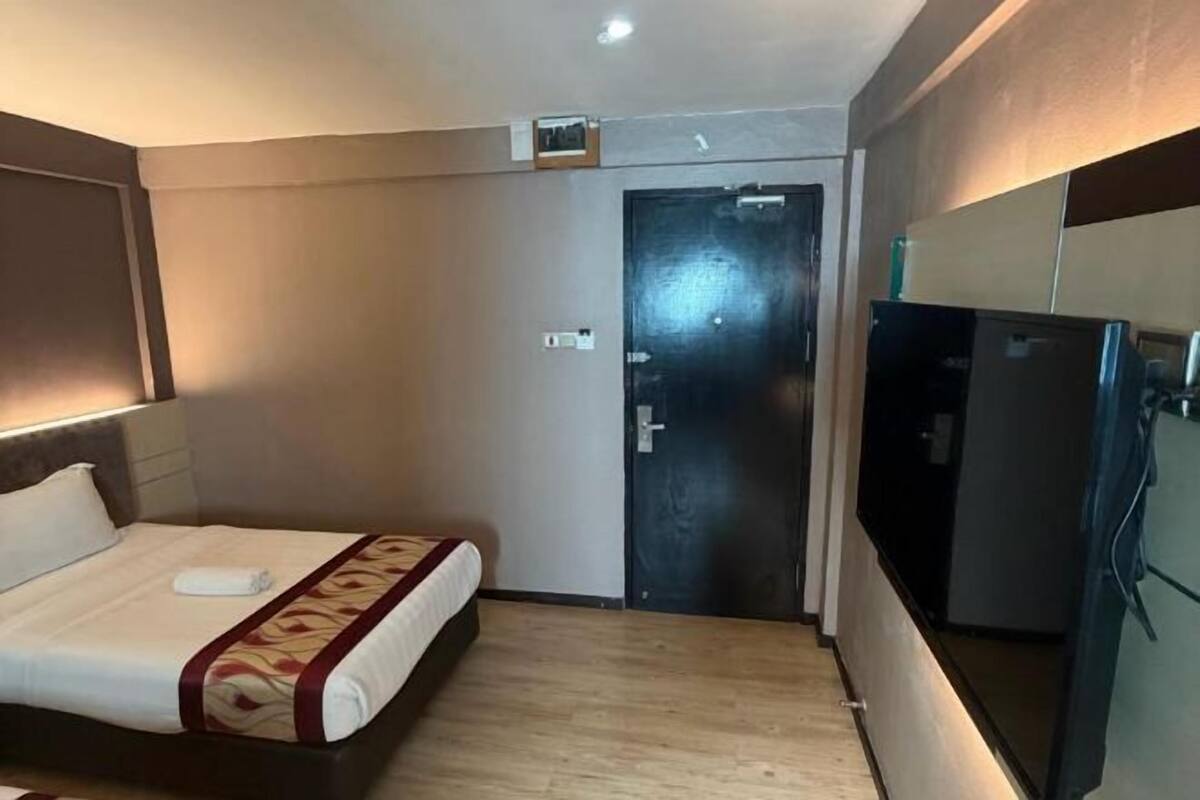 A hotel room with a bed, a door, a refrigerator, and a television.