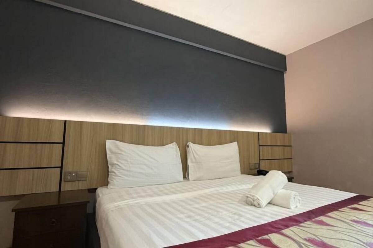 A hotel room with a bed, a nightstand, and a headboard with built-in lighting.