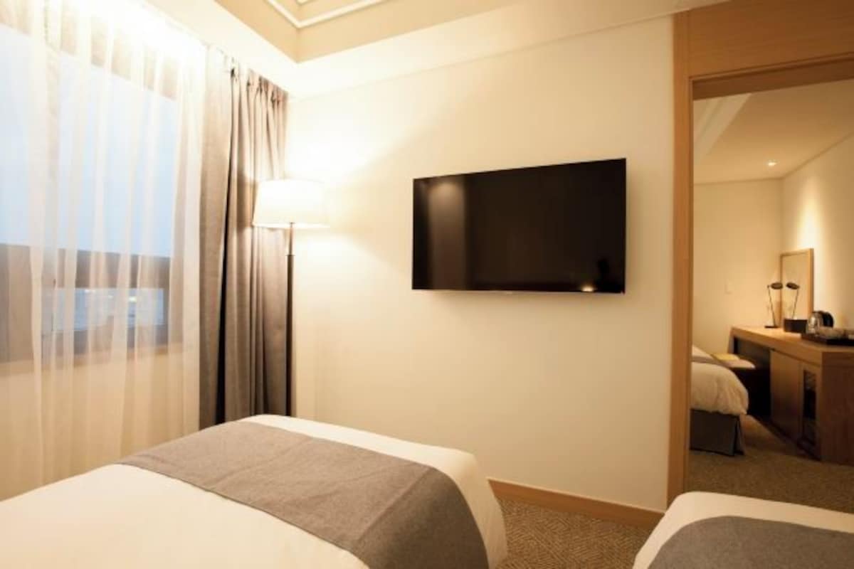 A hotel room with two beds, a flat-screen TV mounted on the wall, and a desk with a chair.
