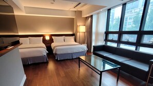 Una habitación de hotel con dos camas, una mesa de centro de vidrio y un ventanal con vistas a la ciudad.