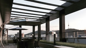Un patio exterior con piso de madera, muebles de mimbre y una banca.