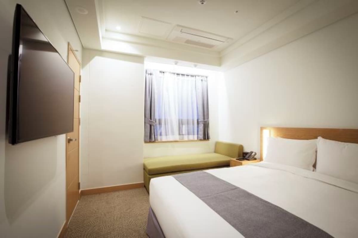 A hotel room with a bed, a seating area, a television, and a window with curtains.