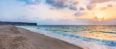 A beach with a rocky cliff, calm waves, and a sunset.