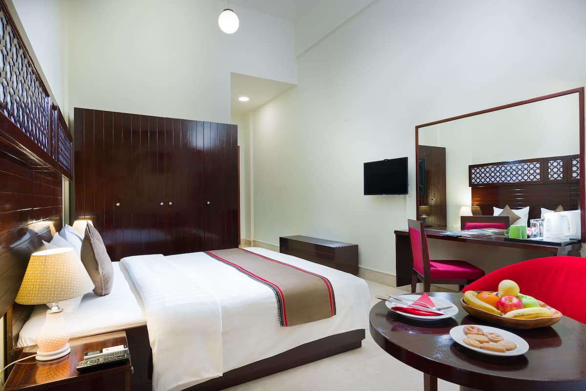 Quarto de hotel com cama, mesa de cabeceira, luminária, cadeira, mesa de jantar e uma fruteira.