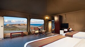 A bedroom with a large bed, a desk, and a chair, with a view of the beach and cliffs. - Ras Al Jinz Turtle Reserve (Al Hadd)
