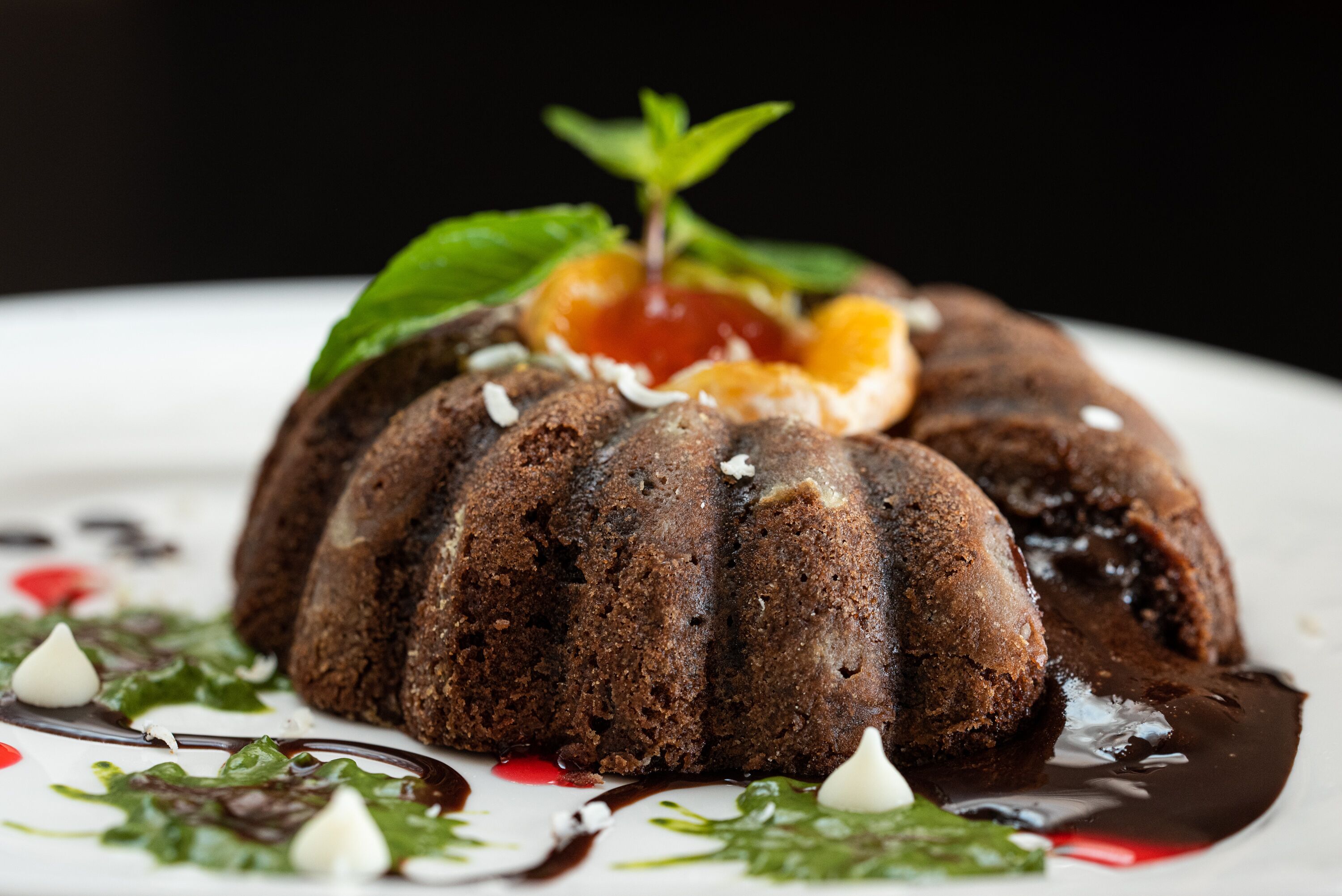 A chocolate bundt cake with a cherry on top, garnished with mint leaves and white cream dots.