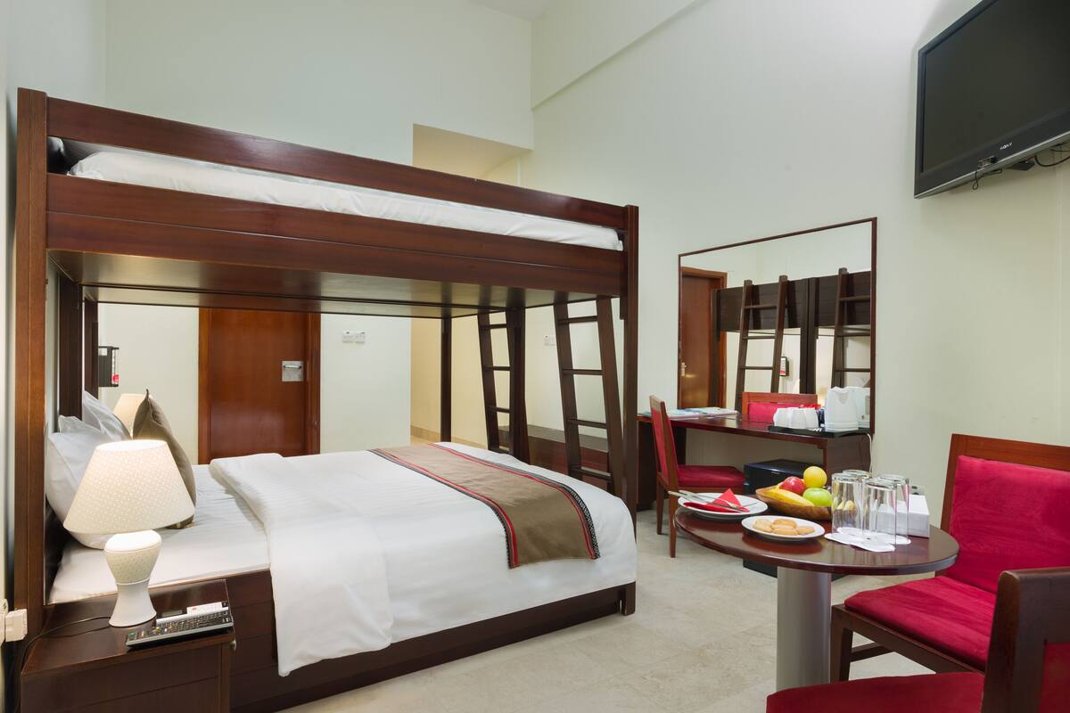 Quarto de hotel com cama de dossel, uma secretária com cadeira, televisão e mesa de jantar com cadeira.