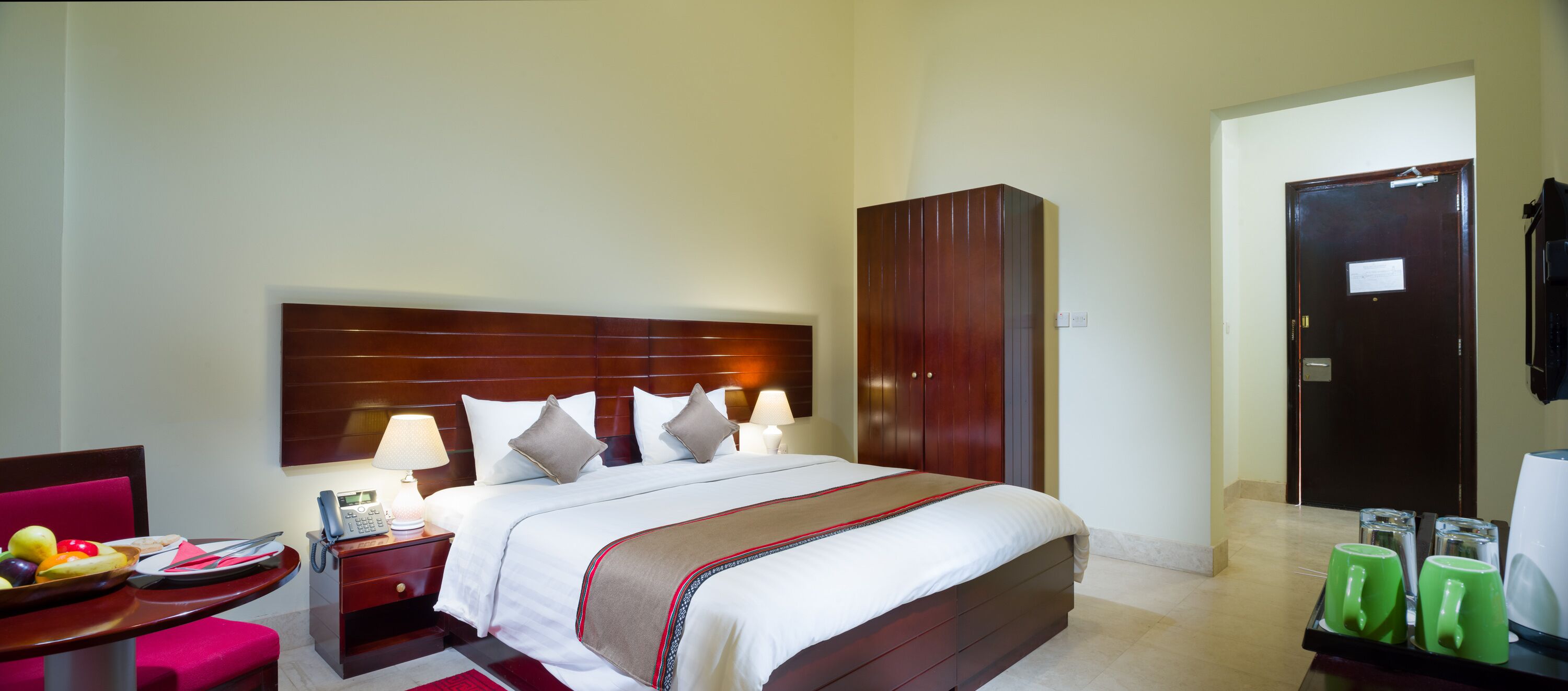 A hotel room with a bed, bedside table, lamp, and a wardrobe.