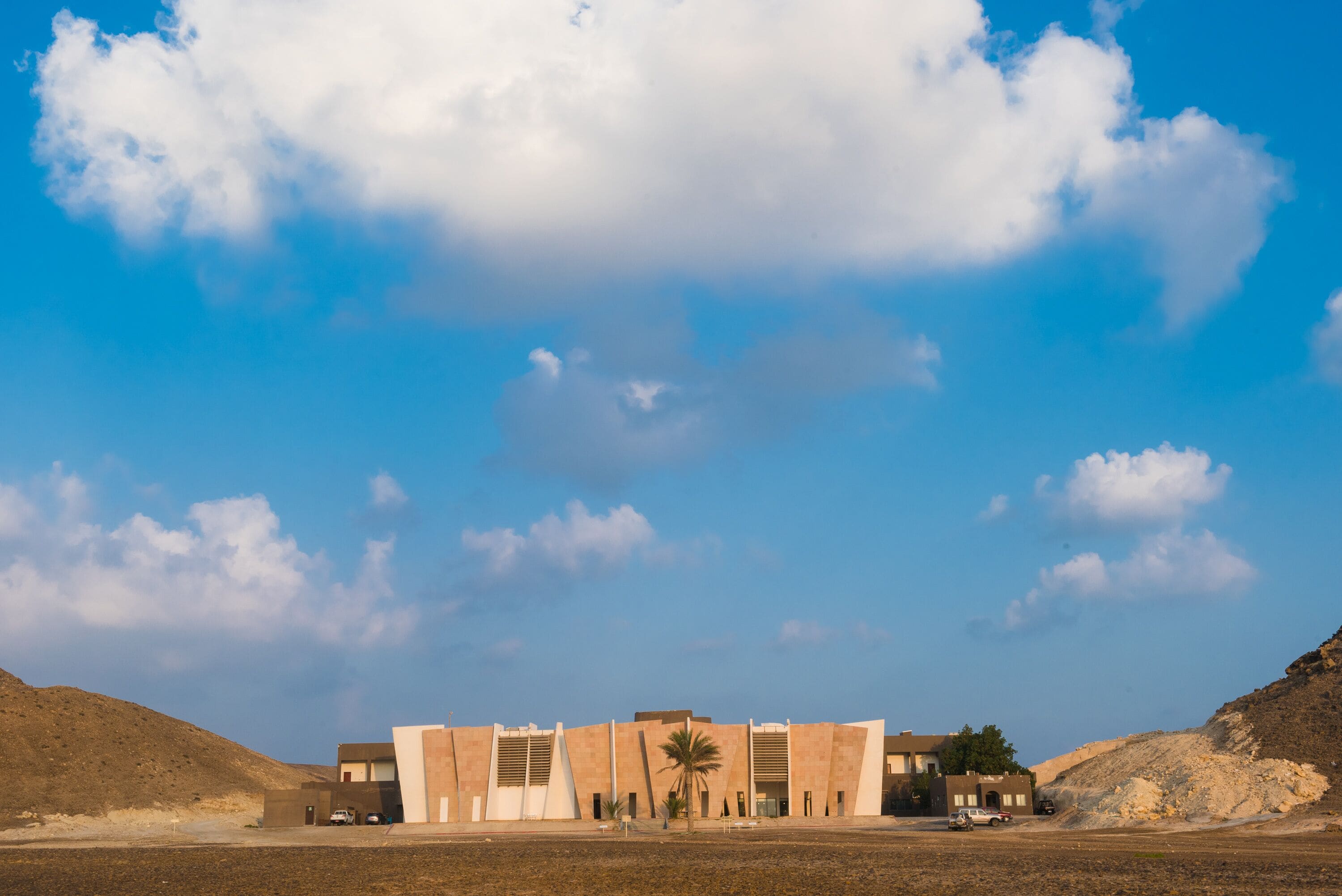A modern building with a flat roof and a symmetrical facade, surrounded by a barren landscape and a clear sky.