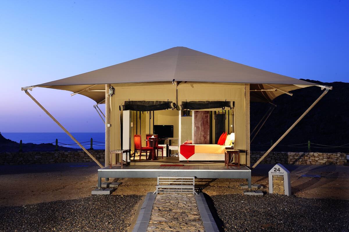 Alojamento em tenda com cama, área de estar e um muro de pedra ao fundo.