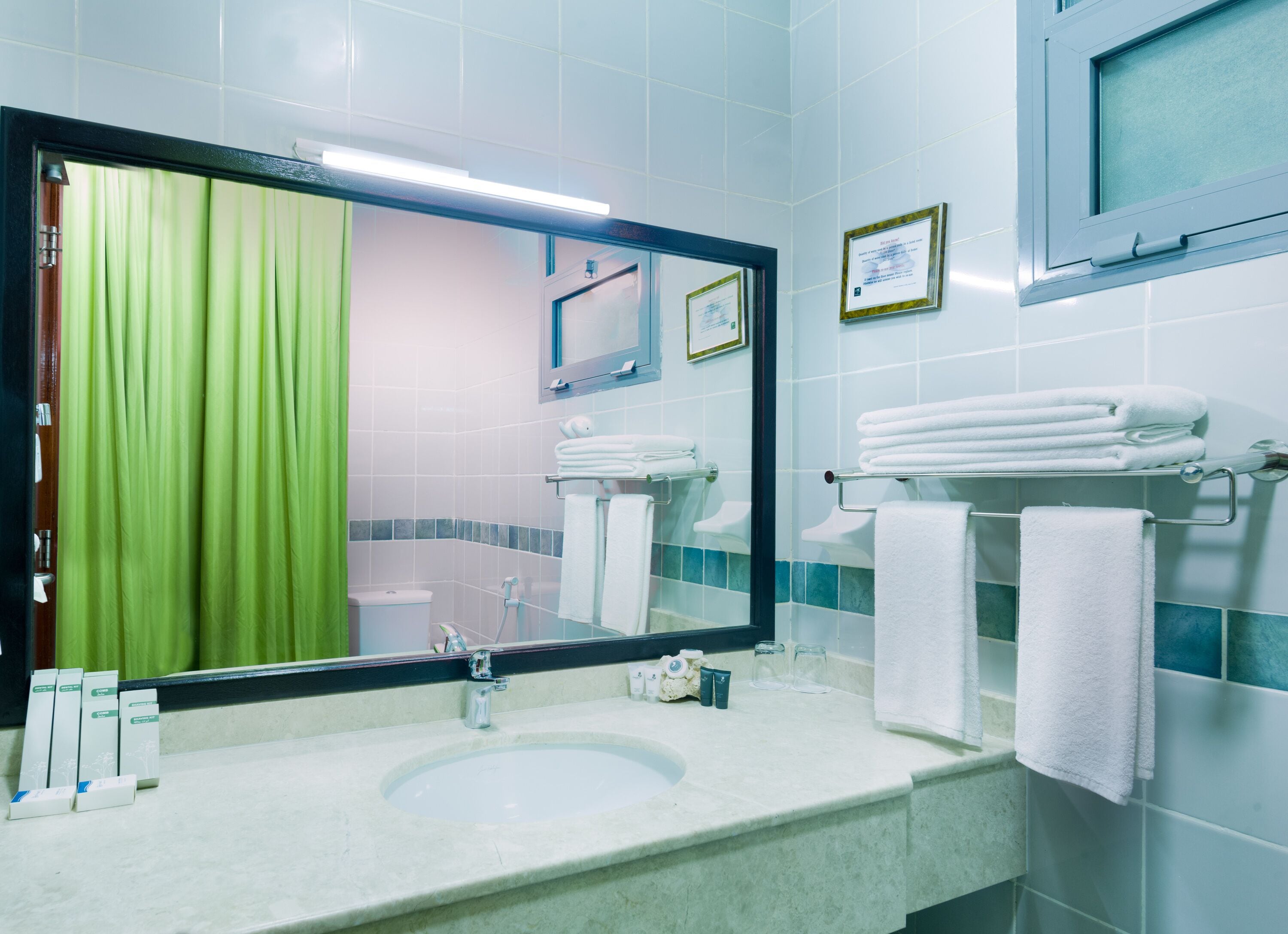 Une salle de bain avec un lavabo, un miroir, un rideau vert et des serviettes blanches.