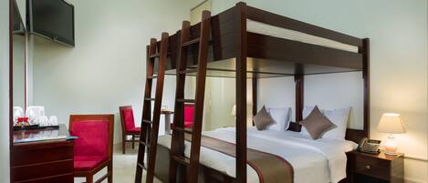 A four-poster bed with a wooden frame, a desk with a chair, a television mounted on the wall, and a bedside table with a lamp.