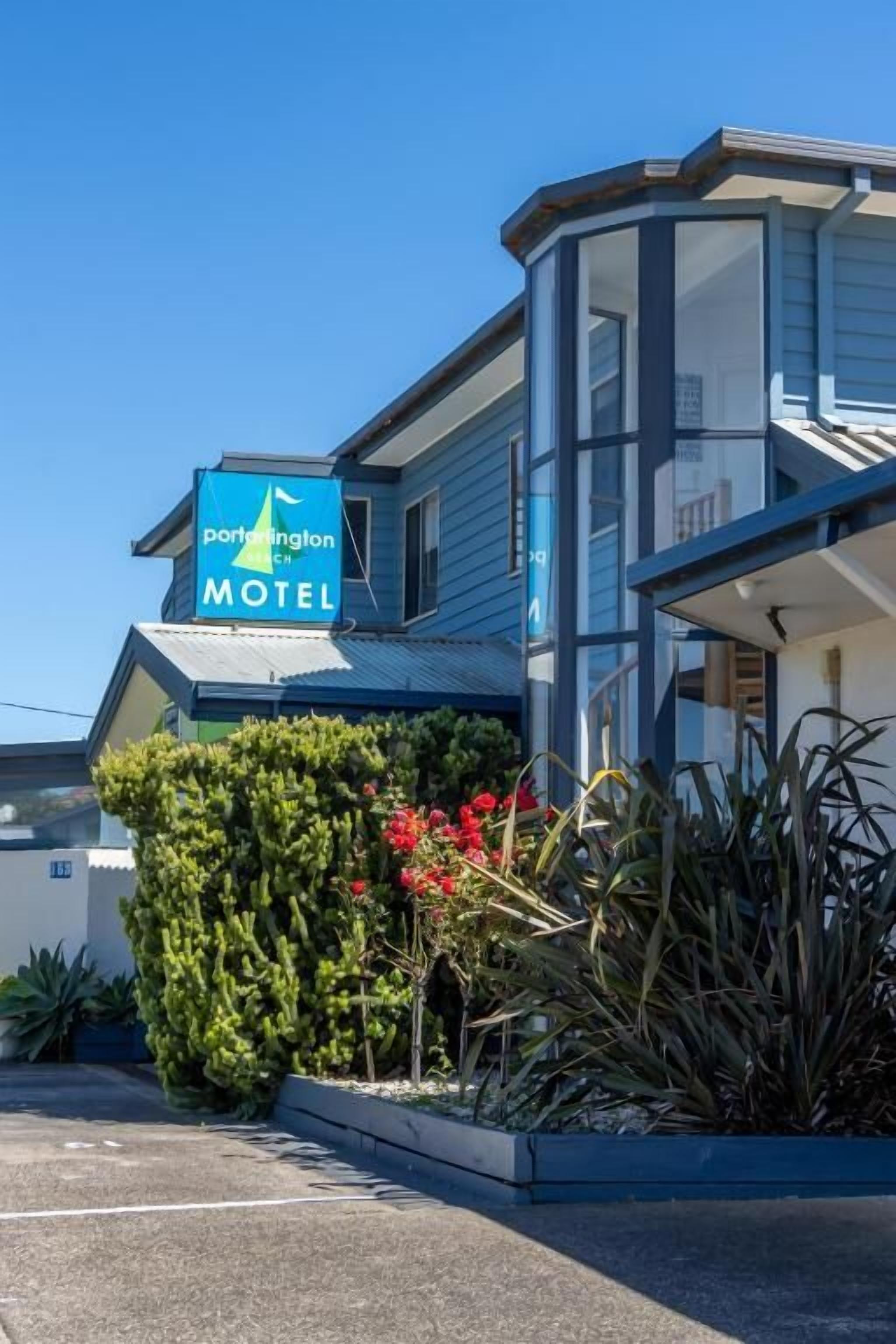A motel with a blue sign, a parking lot, and some landscaping.