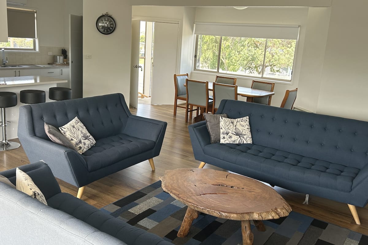Uma sala de estar moderna com dois sofás, uma mesa de centro e uma área de jantar com mesa e cadeiras.