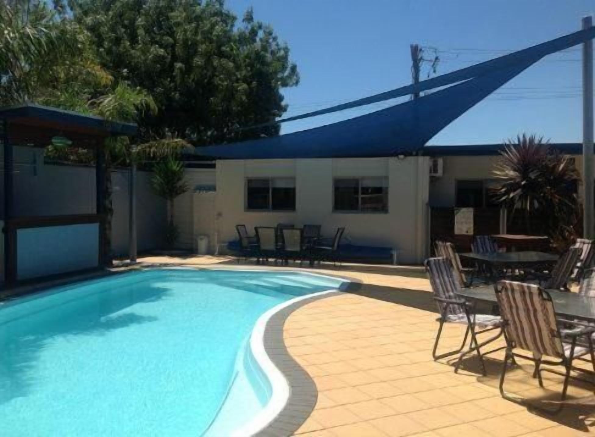A swimming pool with a curved edge, surrounded by a covered patio area with chairs and tables.