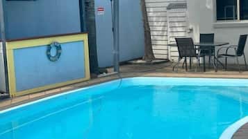 Una piscina con zona techada, una silla y una mesa.