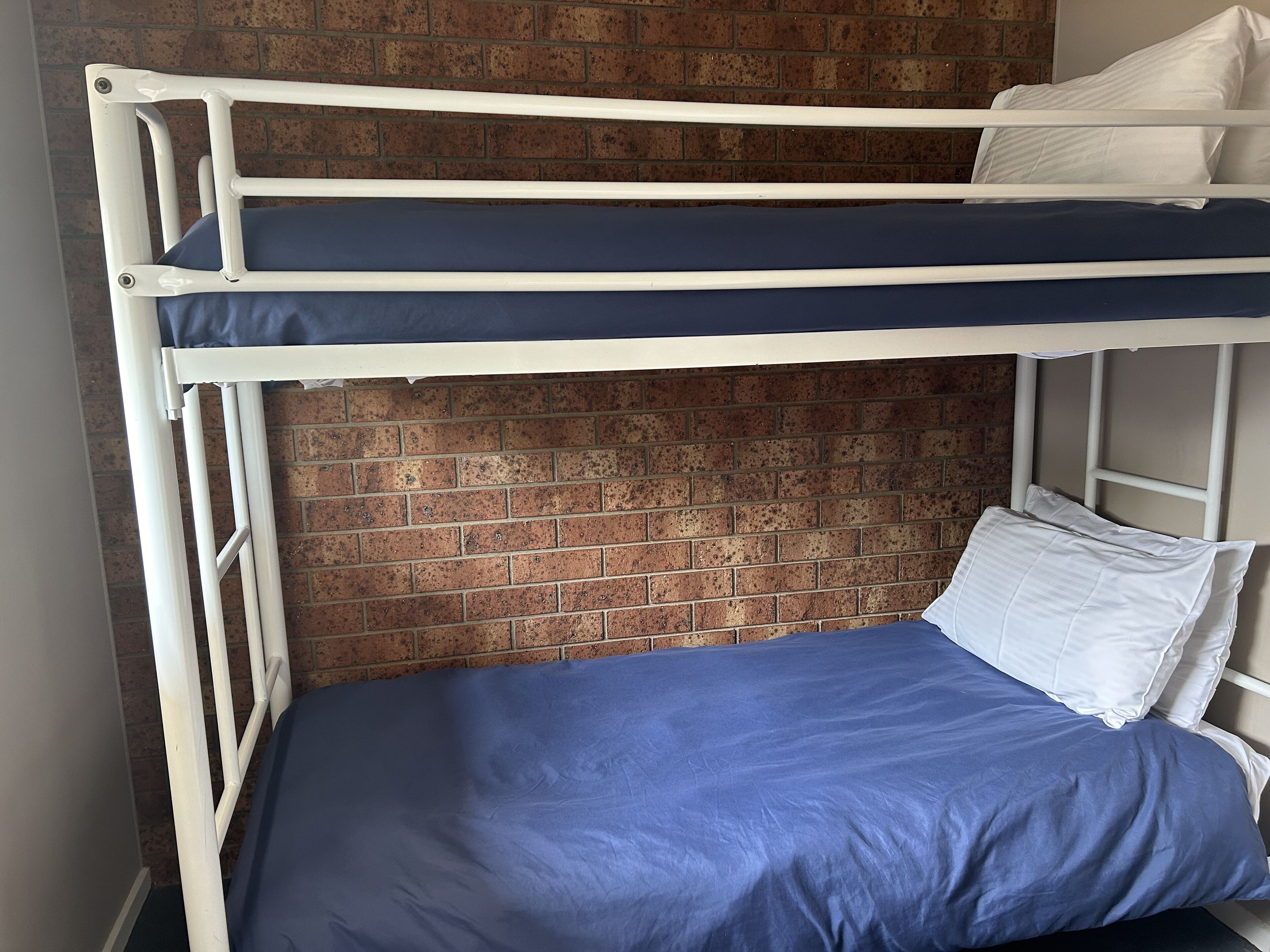 A bunk bed with a blue mattress and white pillows against a brick wall.