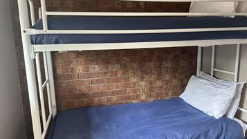 Una cama litera con colchón azul y almohadas blancas, con un muro de ladrillo al fondo.