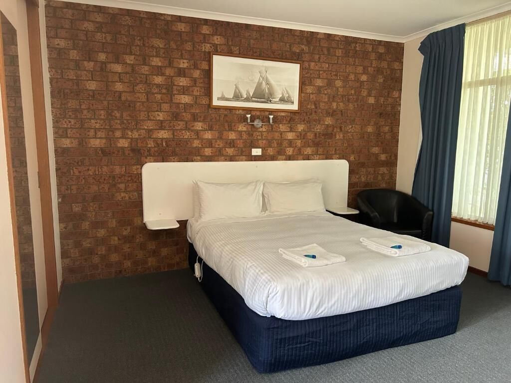 Une chambre d’hôtel avec un mur orné d’un motif en briques, un lit avec du linge de maison blanc, une chaise noire et une fenêtre avec des rideaux bleus.