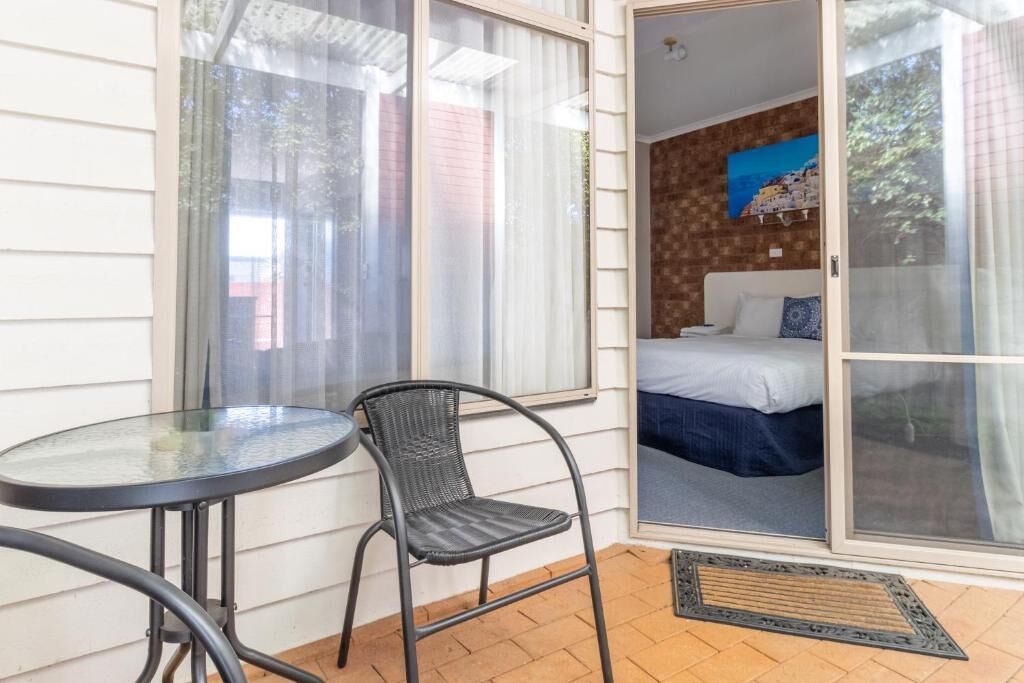 A room with a bed, a chair, a table, and a sliding glass door leading to an outdoor area.