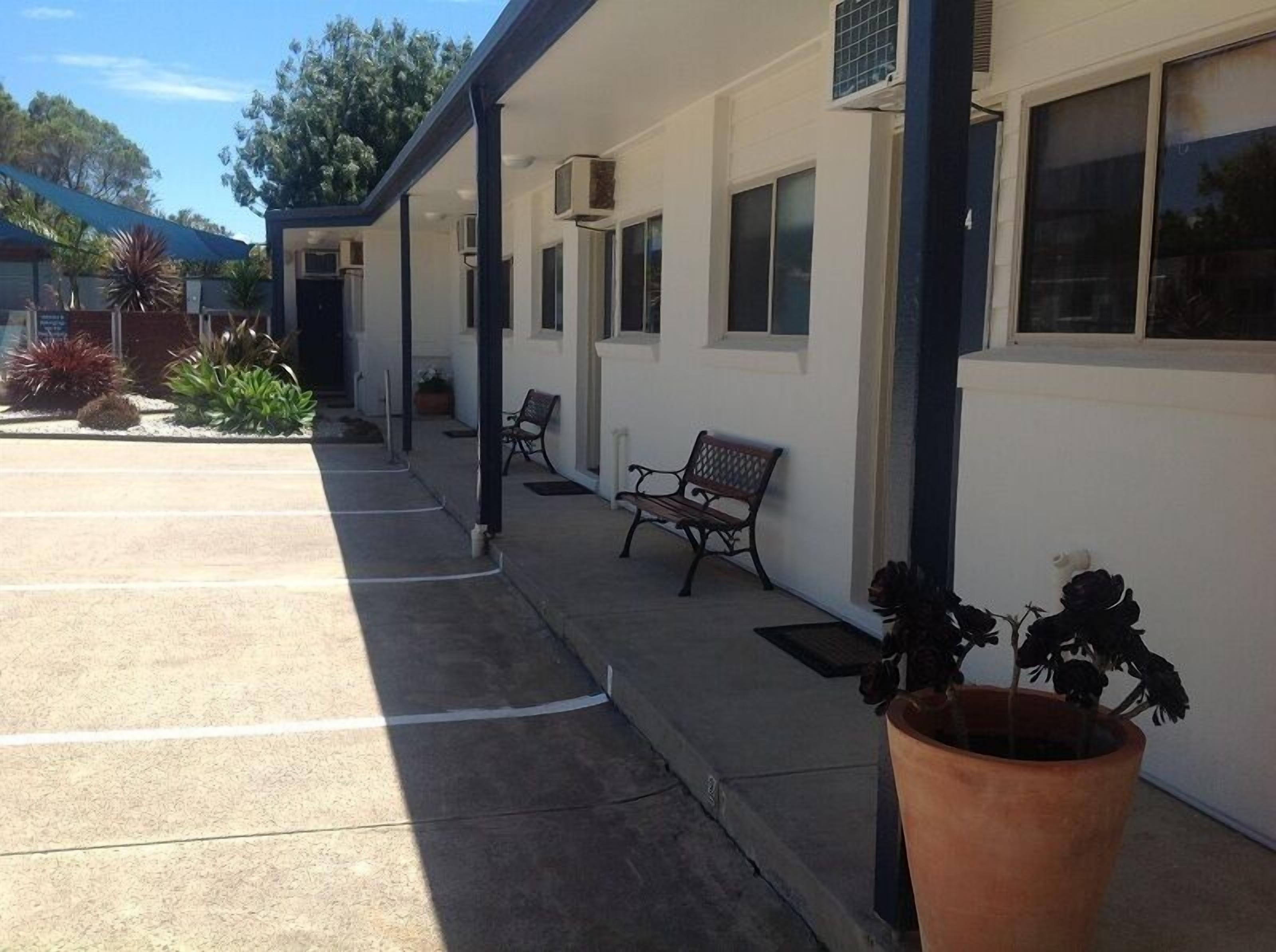 A building with a covered outdoor seating area, air conditioning units, and a potted plant.