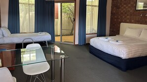 A hotel room with two single beds, a glass table with chairs, a wooden desk, and a brick wall. - Portarlington Beach Motel (Portarlington)
