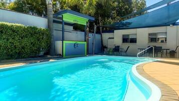 A swimming pool with a curved edge, surrounded by a wooden deck and a covered seating area.