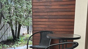 A patio area with two metal chairs and a small round table, wooden slats on the wall, and a brick floor. - Portarlington Beach Motel (Portarlington)