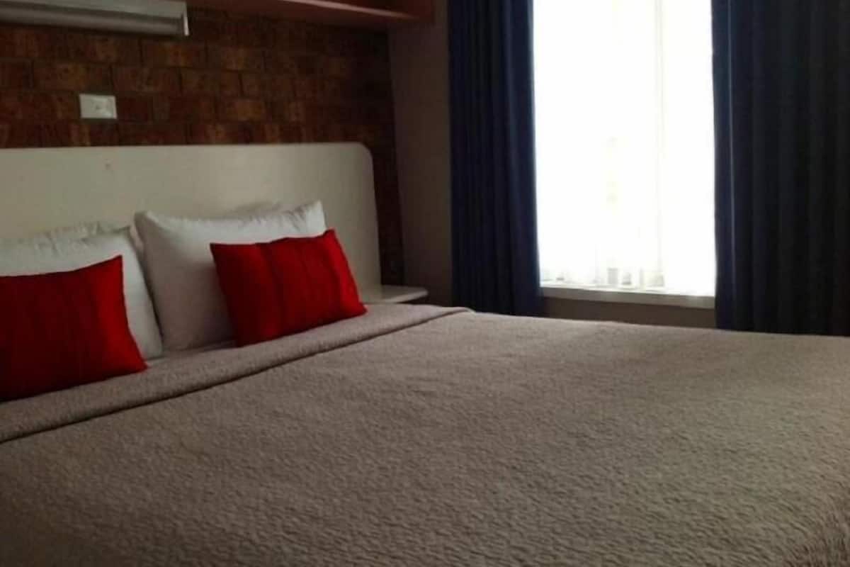 A bed with a headboard, red and white pillows, and a window with curtains.