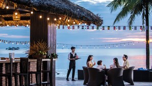 Un área de comedor al aire libre con sillas de mimbre y una barra, con vista al mar.
