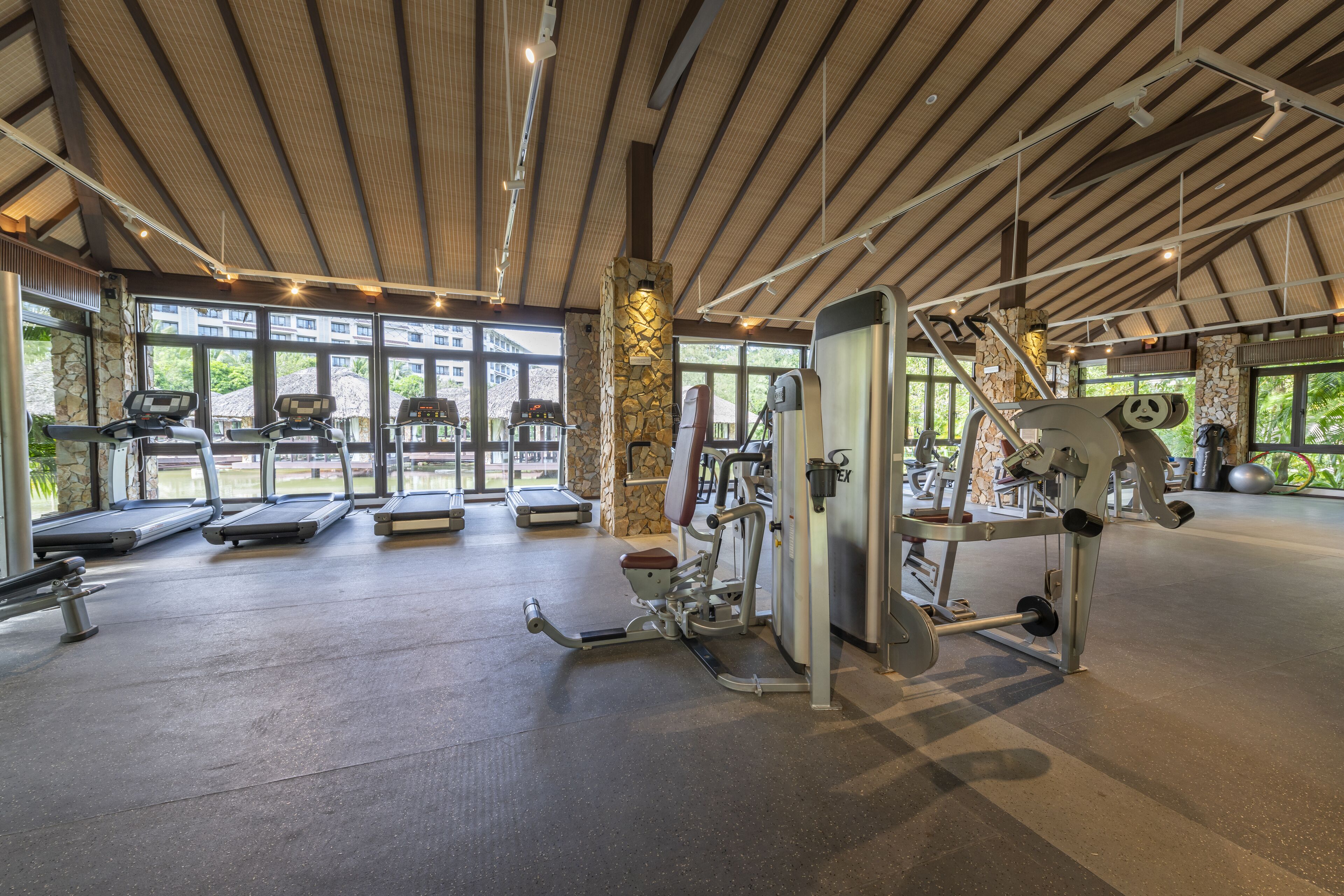 Een ruime fitnessruimte met loopbanden, elliptische trainers en gewichten. Grote ramen zorgen voor daglicht en uitzicht op het omliggende landschap.