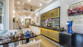 Un restaurante con zona de bar, mobiliario de mimbre blanco y una pared decorativa con un biombo.