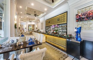 Un restaurante con zona de bar, mobiliario de mimbre blanco y una pared decorativa con un biombo.