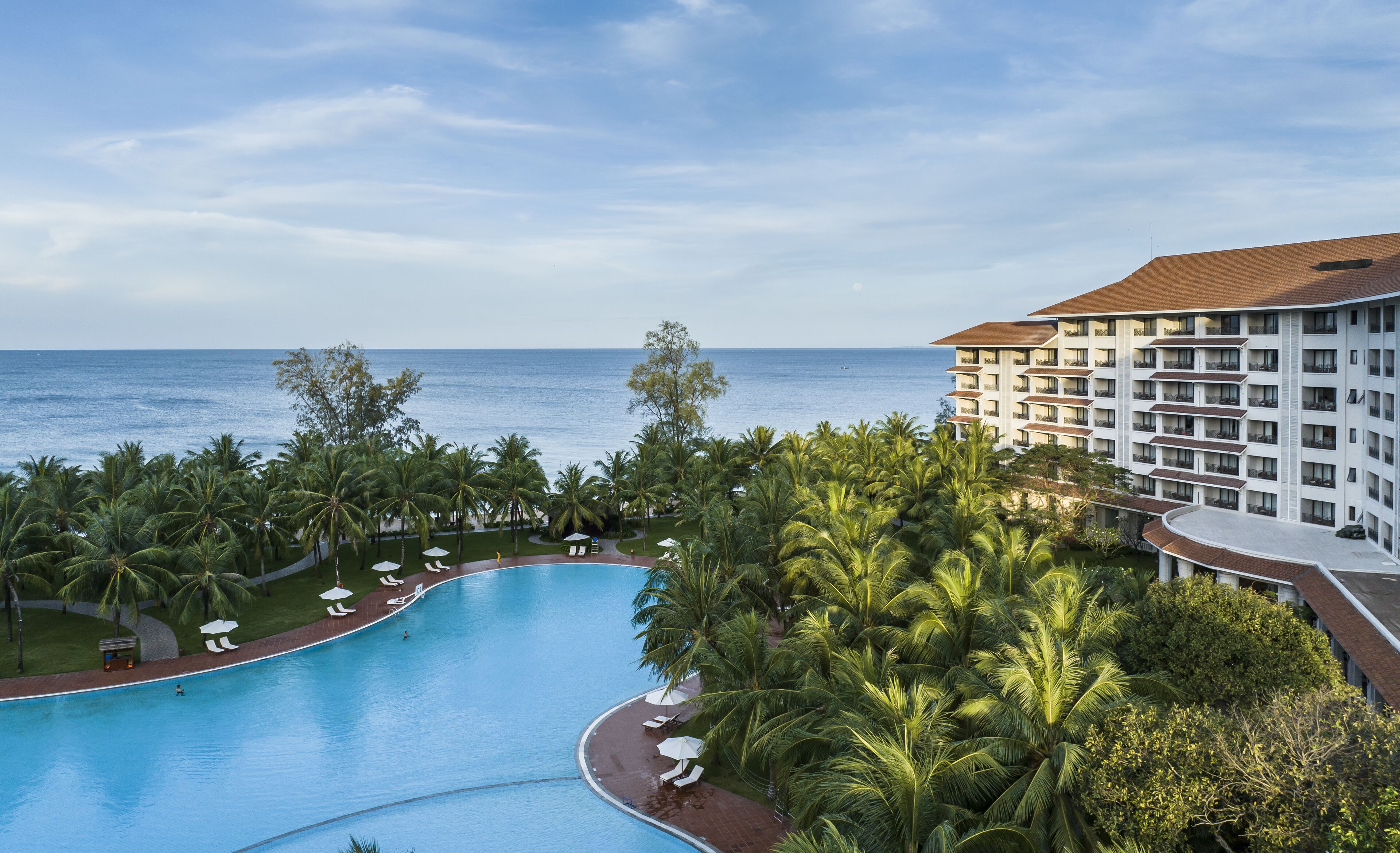 A resort with a large swimming pool, palm trees, and a view of the ocean.