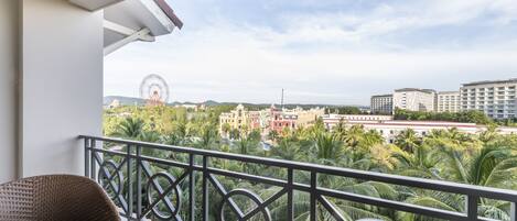 Un balcón con sillas de mimbre y una mesa de cristal, con vistas a un paisaje urbano que incluye edificios y una noria.