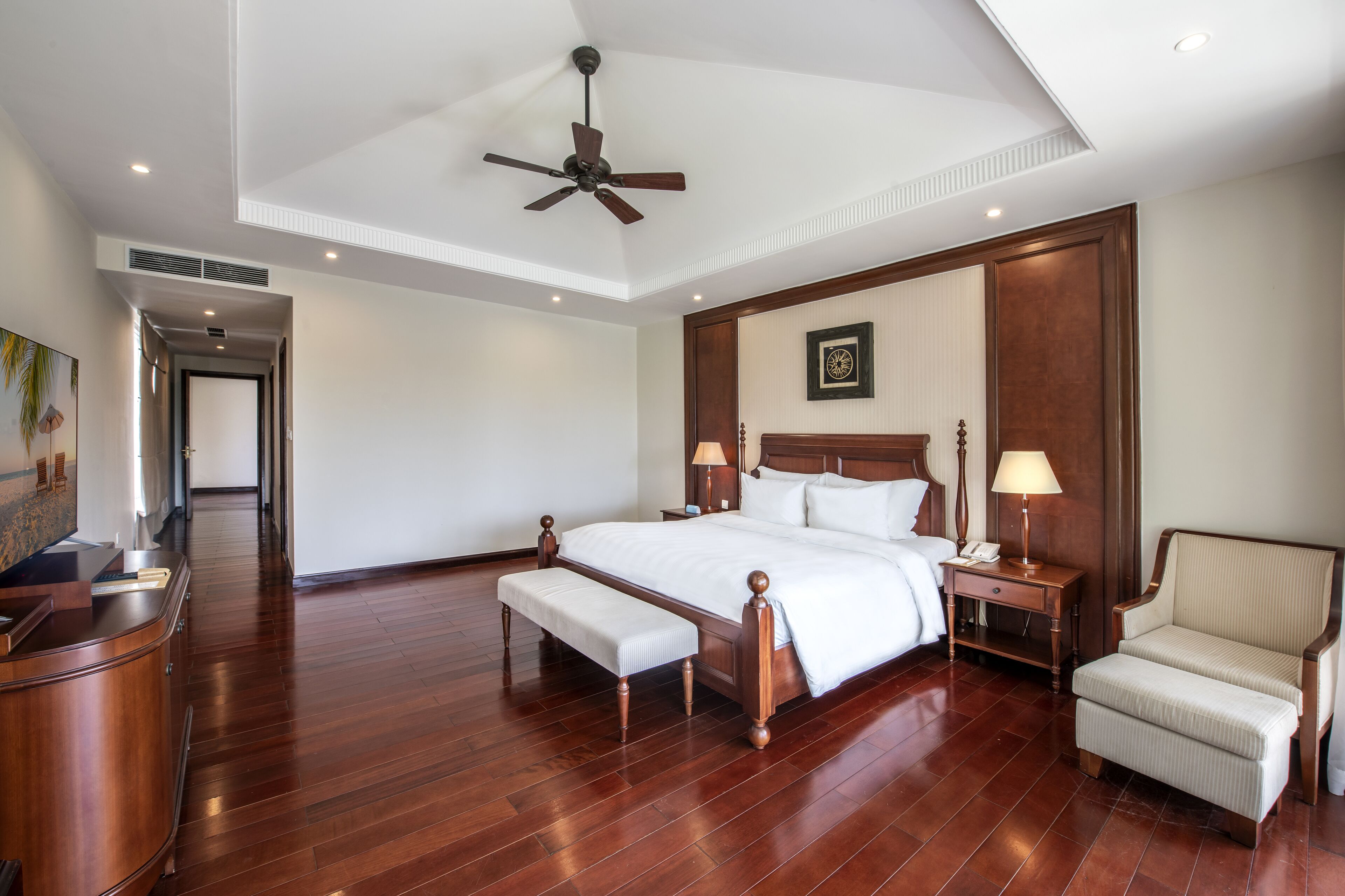 Una habitación de hotel espaciosa con una cama grande, cabecera de madera, zona de estar con una silla, un escritorio y un banco.