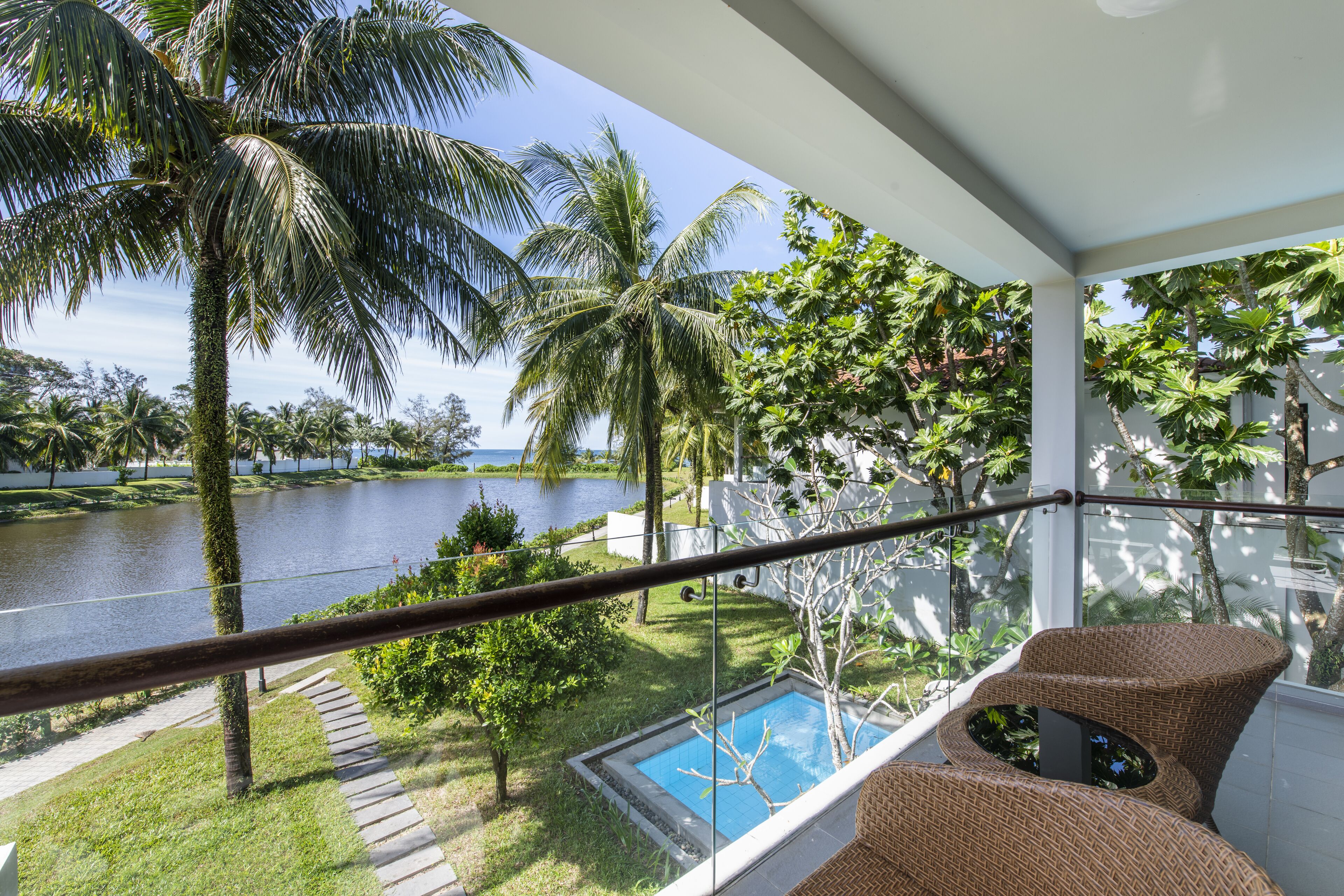 A balcony with a view of a lake, a swimming pool, and wicker furniture.