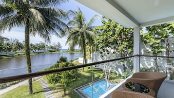 Un balcón con vista a un lago, una piscina y muebles de mimbre.
