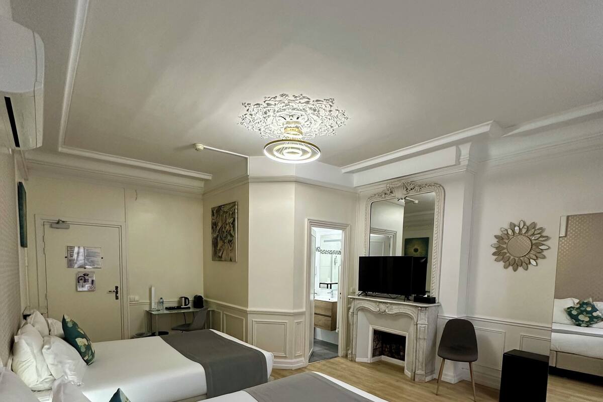 A hotel room with two beds, a desk, a television, and a fireplace.