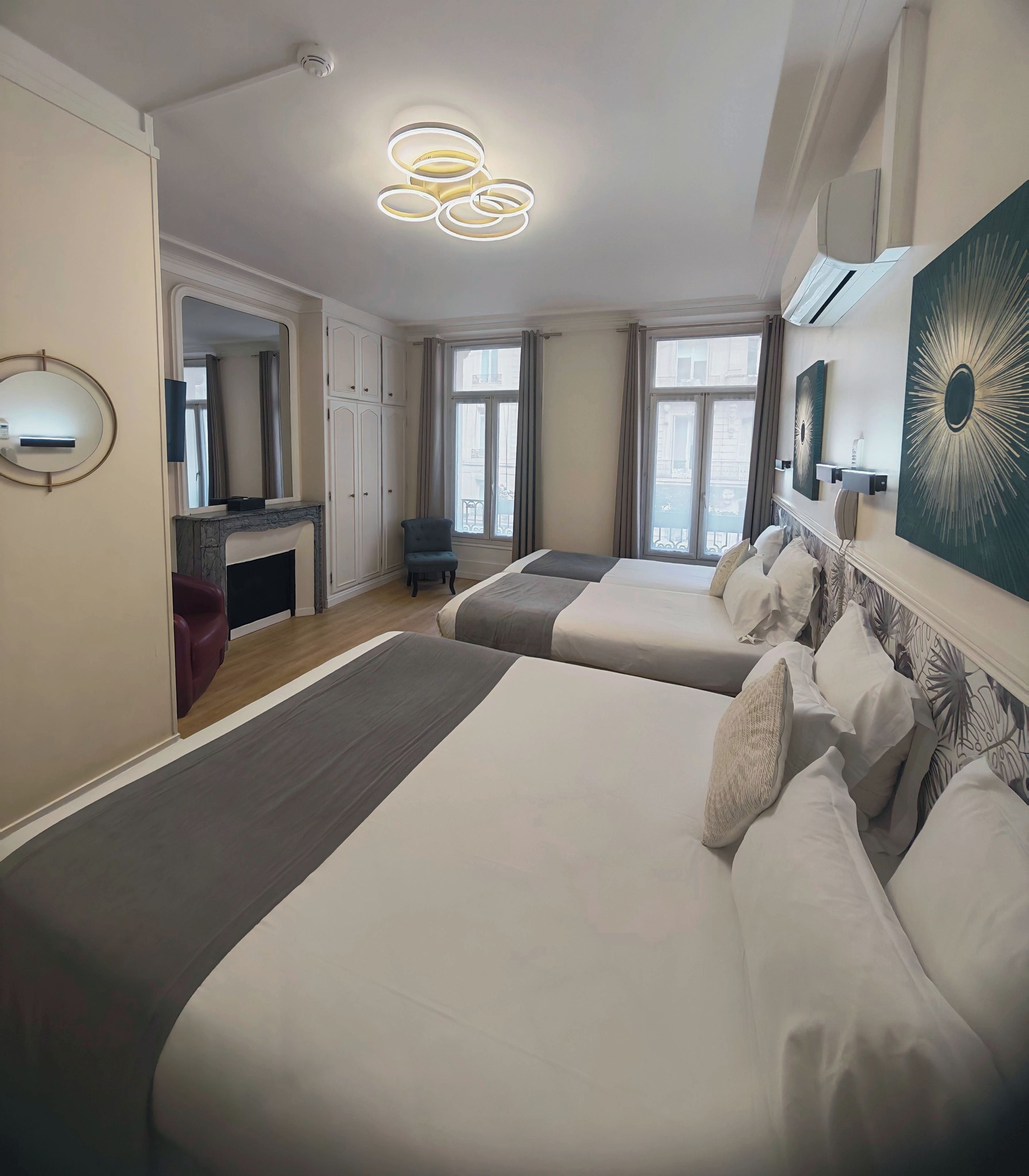 A hotel room with two beds, a sitting area with a chair, a fireplace, and a large window with curtains.