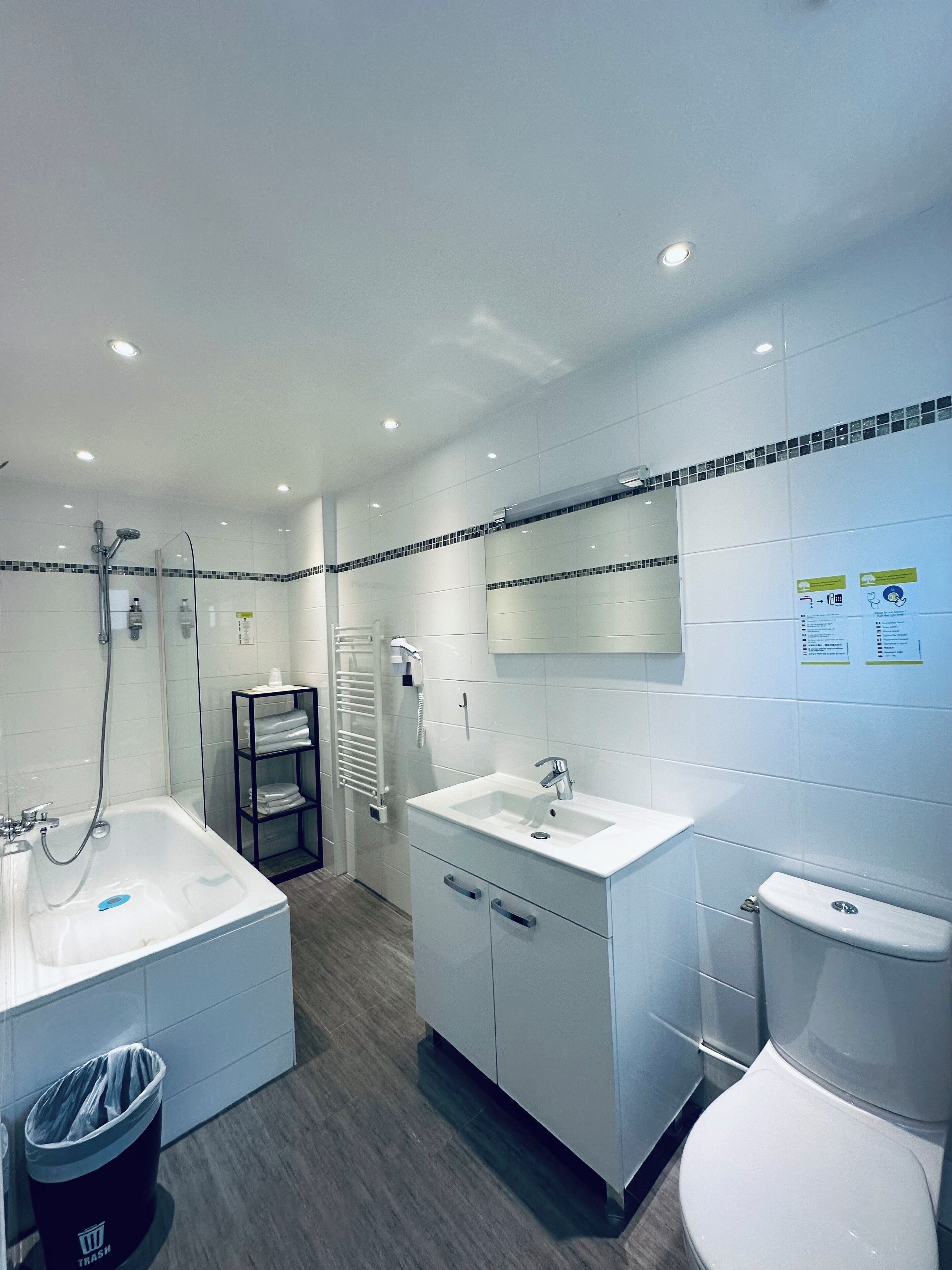 A modern bathroom with a bathtub, a sink, and a toilet. There is a towel rack and a trash bin.